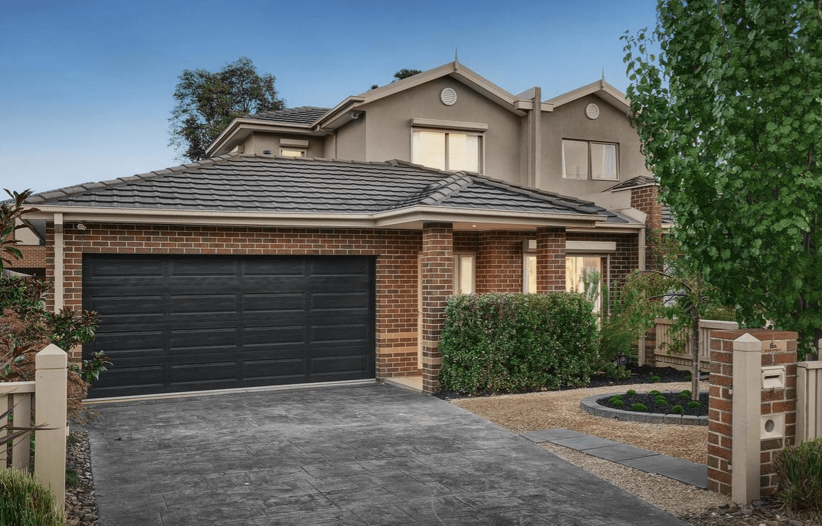 Two-story brick suburban house with a large dark two-car garage and a landscaped front yard.