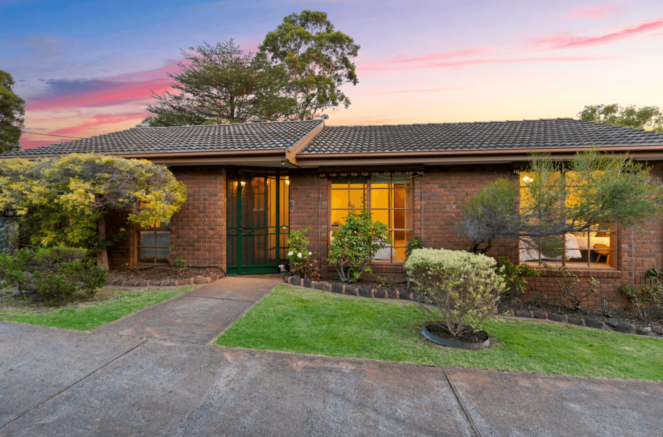Recent Purchase Image - Marsden Buyers Agents Brick ranch-style house with a tiled gray roof at sunset, front yard shrubs, and a paved driveway.