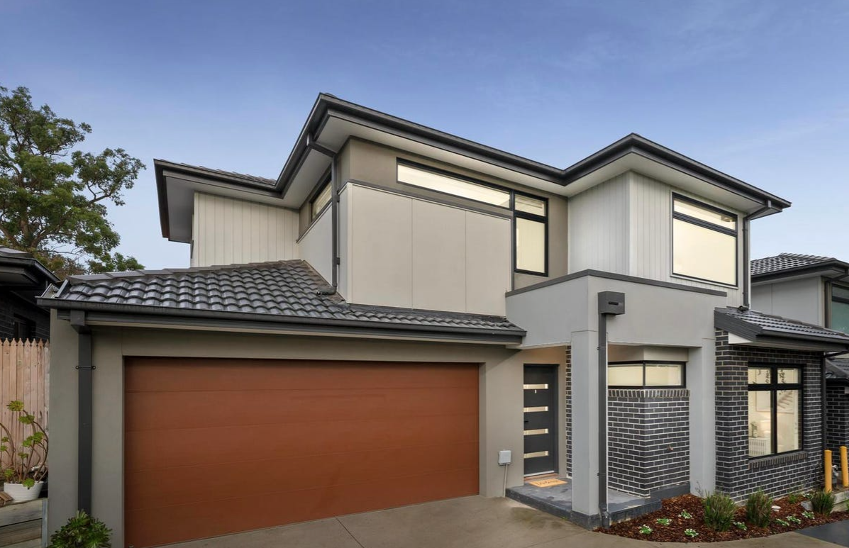 Modern two-story house with a large brown garage door and a narrow front entry under a covered porch.
