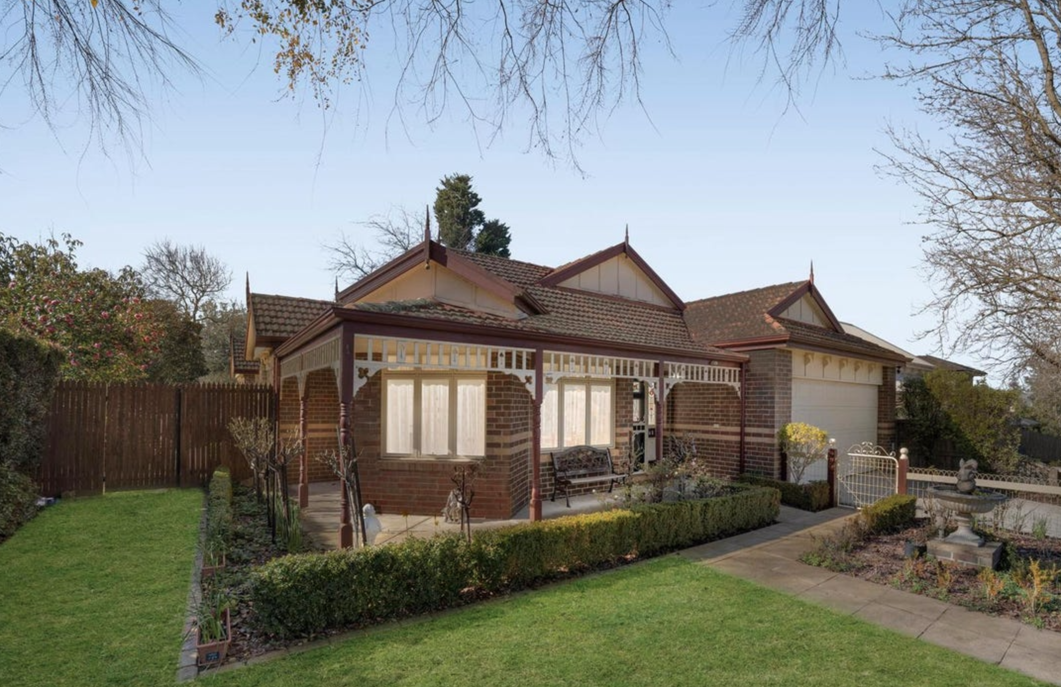Brick bungalow with a red-tiled roof, white trim and a covered porch, set in a manicured front yard under a clear blue sky.